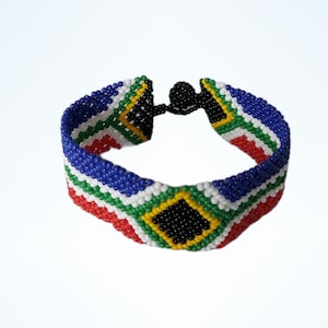 May include: A beaded bracelet with the South African flag design. The bracelet displays a pattern of blue, white, red, green, yellow, and black beads. It has a black clasp and is designed to be worn around the wrist.