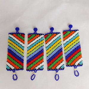 May include: Four beaded rectangular ornaments with a vibrant, diagonal striped pattern in red, orange, yellow, green, blue, and white. Each ornament has a blue loop at the bottom and a blue bead at the top. The background is plain white.