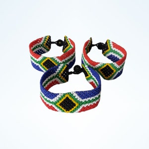 May include: Three beaded bracelets with a South African flag design. The bracelets feature red, white, blue, green, yellow, and black beads. Each bracelet has a black clasp. The bracelets are displayed against a white background.