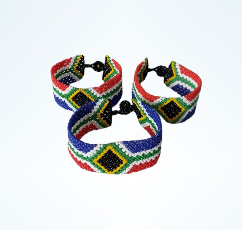 May include: Three beaded bracelets with a South African flag design. The bracelets feature red, white, blue, green, yellow, and black beads. Each bracelet has a black clasp. The bracelets are displayed against a white background.