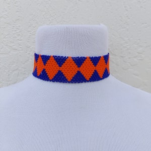 May include: A beaded choker necklace with a geometric pattern. The choker features a repeating diamond design in orange and blue. The necklace is displayed on a white mannequin neck.