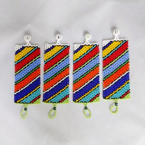 May include: Four beaded bracelets with a rectangular shape and a colorful striped pattern. The bracelets feature a white top, a green bottom, and a loop. The stripes include red, orange, yellow, blue, and turquoise beads.