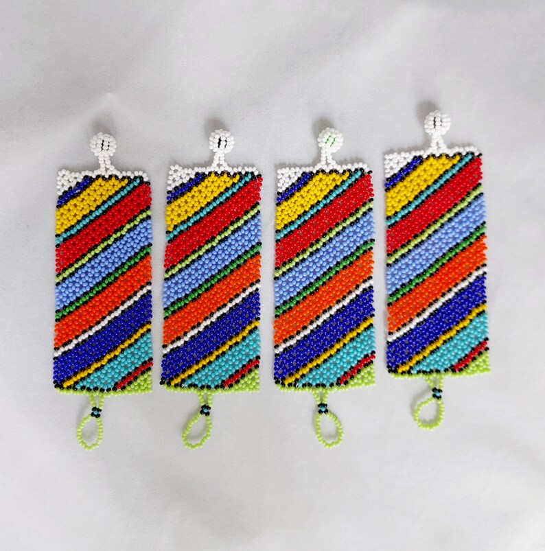 May include: Four beaded bracelets with a rectangular shape and a colorful striped pattern. The bracelets feature a white top, a green bottom, and a loop. The stripes include red, orange, yellow, blue, and turquoise beads.