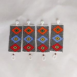 May include: Four beaded bracelets with a black background and colorful diamond patterns in red, orange, blue, and green. Each bracelet has a white loop at the bottom and a white bead at the top.