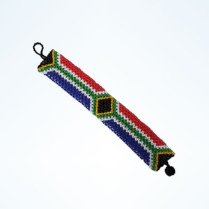 May include: Beaded bracelet with the South African flag design. The bracelet has a black loop and a black tassel. The design includes red, green, blue, yellow, and white beads. The bracelet is approximately 20 cm long.