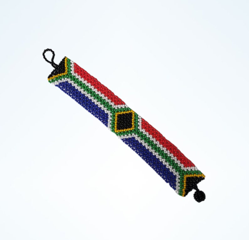 May include: Beaded bracelet with the South African flag design. The bracelet has a black loop and a black tassel. The design includes red, green, blue, yellow, and white beads. The bracelet is approximately 20 cm long.