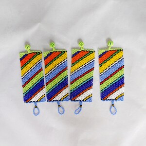 May include: Four beaded bookmarks with a colorful striped pattern. The bookmarks feature a variety of colors, including red, orange, yellow, green, blue, and white. Each bookmark has a small loop at the bottom and a green beaded top.