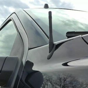 May include: Black Ford F-150 XLT truck. The image shows the side of the truck, including the door, mirror, and antenna. The F-150 and XLT emblems are visible. The paint is glossy, reflecting the surroundings.