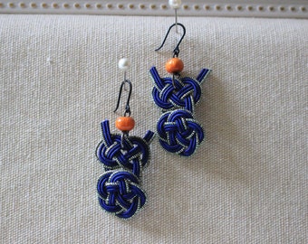 May include: A pair of blue and silver earrings with orange beads. The earrings are made of knotted cord and have a dangling design.