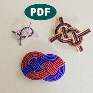 以下が含まれることがあります： カラフルな紐で作った装飾的な結び目が3種類。結び目は、赤、青、黒、白、金など、さまざまなパターンと色で結ばれています。