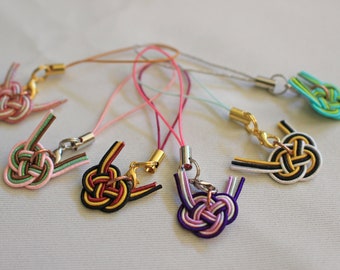 May include: Six colorful phone charms with intricate knotted designs. Each charm features a different color combination of pink, green, red, black, white, and purple.