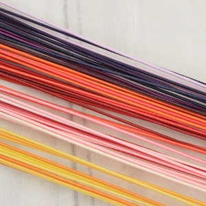 Könnte beinhalten: Eine Sammlung bunter Schnüre in den Farben Lila, Orange, Rot, Rosa und Gelb. Die Schnüre sind in einem Farbverlauf angeordnet, wobei die dunkelsten Farben oben und die hellsten Farben unten sind.