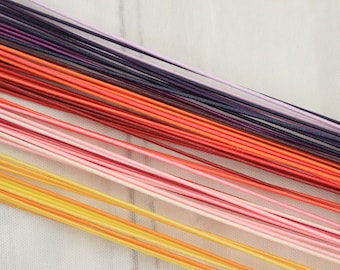 May include: A collection of thin, smooth, round cords arranged in a parallel diagonal pattern. The cords feature a vibrant gradient color palette, transitioning from bright yellow and gold to soft pink, coral, deep red, orange, and dark purple.