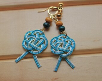 May include: A pair of blue and white earrings with a knot design. The earrings are made with gold-tone metal and have wooden beads.