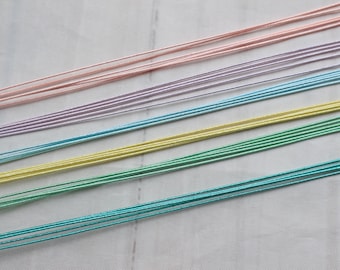 May include: A collection of embroidery floss in various pastel colors, including pink, lavender, light blue, yellow, and green. The floss is arranged in parallel lines on a white surface.