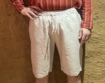 May include: Beige shorts featuring an elasticated waistband with a matching drawstring tie. The shorts are crafted from a textured fabric and fall to just above the knee, providing a relaxed fit with a simple, clean design for casual wear.