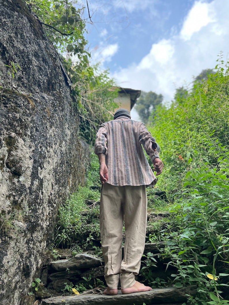 May include: A person wearing a striped shirt and beige pants walks up a stone staircase in a lush green forest setting.