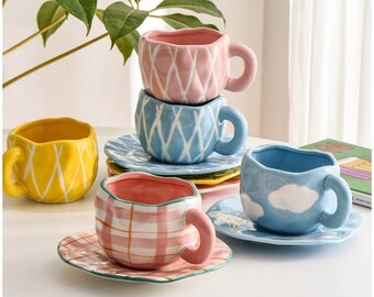 May include: A collection of colorful ceramic teacups and saucers. The cups feature various designs, including diamond patterns, plaid, and cloud motifs. Colors include yellow, pink, blue, and white. The cups have rounded handles and sit on matching saucers.