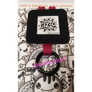 May include: Black phone grip with a black ring and a red strap. The grip has the text "GIZ-O Phone-Hoop" on a white label. The background features a black and white doodle design with various cartoon characters.
