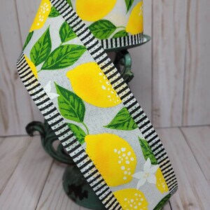 Puede incluir: Cinta decorativa con dise&ntilde;o de limones. La cinta presenta limones amarillos, hojas verdes y flores blancas sobre un fondo gris claro. Bordes a rayas blancas y negras enmarcan los bordes de la cinta.