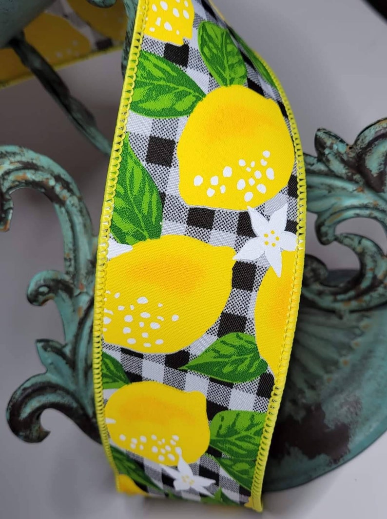 Puede incluir: Cinta decorativa con un patr&oacute;n repetido de limones amarillos brillantes, hojas verdes y flores blancas sobre un fondo a cuadros blanco y negro. La cinta tiene un borde cosido amarillo. Ideal para manualidades y decoraci&oacute;n.