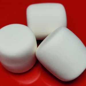 May include: Three white, cylindrical marshmallows arranged on a bright red surface. The marshmallows have a smooth, rounded shape, with a slightly irregular form. The image is a close-up, highlighting the texture and color contrast.