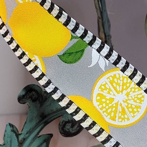 Puede incluir: Primer plano de una cinta con un patr&oacute;n de limones. La cinta presenta limones amarillos brillantes, hojas verdes y rodajas de lim&oacute;n sobre un fondo gris claro. Los bordes est&aacute;n adornados con rayas blancas y negras. La cinta se utiliza probablemente para manualidades o decoraci&oacute;n.