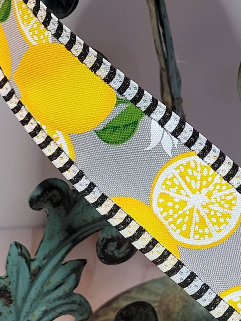 Puede incluir: Primer plano de una cinta con un patr&oacute;n de limones. La cinta presenta limones amarillos brillantes, hojas verdes y rodajas de lim&oacute;n sobre un fondo gris claro. Los bordes est&aacute;n adornados con rayas blancas y negras. La cinta se utiliza probablemente para manualidades o decoraci&oacute;n.