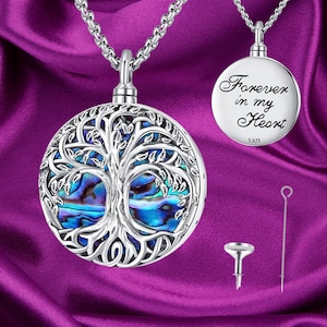 Może przedstawiać: Srebrny naszyjnik z zawieszką w kształcie drzewa życia, ozdobioną niebieską i zieloną wkładką z abalonu. Na odwrocie zawieszki znajduje się napis "Forever in my Heart" z inskrypcją "S925". Naszyjnik jest dostarczany z małym lejkiem i narzędziem do napełniania zawieszki.