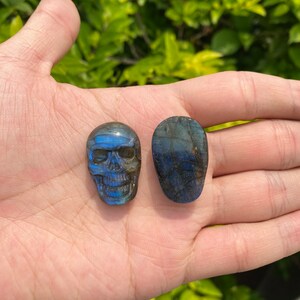 Puede incluir: Dos cr&aacute;neos de cristal de labradorita, uno tallado en forma de cr&aacute;neo y el otro de forma ovalada lisa. Ambos son de color azul oscuro con destellos iridiscentes.