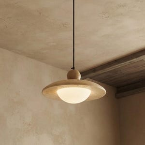 May include: A pendant light fixture featuring a circular light-colored wood canopy, a thin black metal rod, and a wide, flat wooden disc shade. A spherical wooden accent sits above the shade, which houses a central, glowing white glass globe.