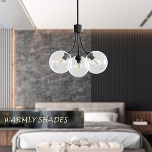 May include: A black modern chandelier with four clear glass globe shades. The chandelier is hanging in a bedroom with a bed and a bench.