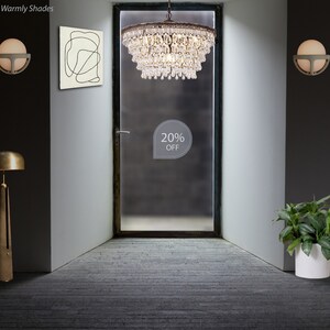 May include: A large, multi-tiered crystal chandelier hangs from the ceiling in a hallway with a frosted glass door. The chandelier has a brass finish and is adorned with crystal drops. A sign on the door reads "20% OFF".