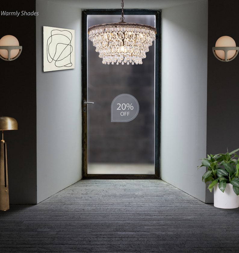 May include: A large, multi-tiered crystal chandelier hangs from the ceiling in a hallway with a frosted glass door. The chandelier has a brass finish and is adorned with crystal drops. A sign on the door reads "20% OFF".