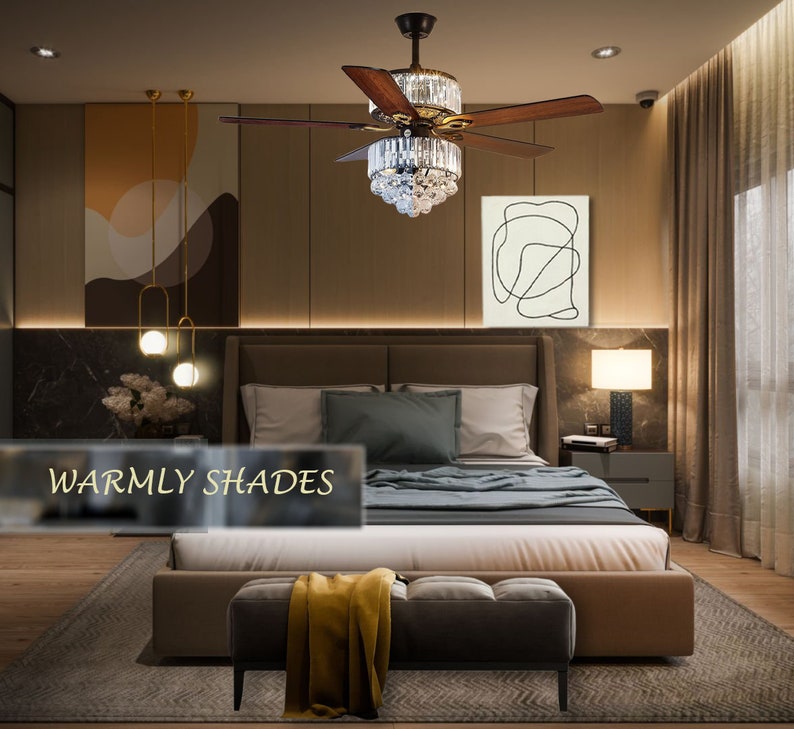 Puede incluir: Un dormitorio con una cama grande, un otomano marr&oacute;n y un ventilador de techo con una l&aacute;mpara de ara&ntilde;a de cristal. Las paredes son de color marr&oacute;n c&aacute;lido y la ropa de cama es blanca y gris. La habitaci&oacute;n tiene un ambiente moderno y elegante. El texto "Warmly Shades" es visible en la imagen.