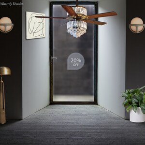 Puede incluir: Un ventilador de techo marr&oacute;n con detalles de cristal cuelga en una habitaci&oacute;n con una pared blanca y una puerta. El ventilador tiene aspas de madera y una l&aacute;mpara de ara&ntilde;a de cristal. Un cartel en la puerta dice "20% DE DESCUENTO".