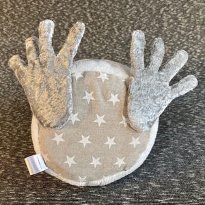 Peut inclure: Une t&ecirc;te de renne en peluche grise avec un dos en tissu blanc orn&eacute; d'un motif d'&eacute;toiles blanches sur fond beige.