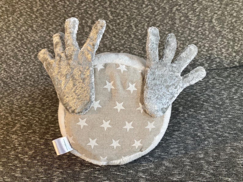 Peut inclure: Une t&ecirc;te de renne en peluche grise avec un dos en tissu blanc orn&eacute; d'un motif d'&eacute;toiles blanches sur fond beige.