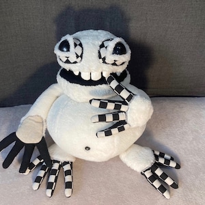 May include: White plush toy with black and white checkered arms and legs. The toy has a large, white, furry body with a black face and large, black eyes. The toy is smiling with a wide, toothy grin.