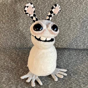 Peut inclure: Un jouet en peluche blanc avec de grands yeux noirs et un large sourire. Le jouet a des oreilles &agrave; carreaux noirs et blancs et de longs bras et jambes blancs &agrave; griffes.