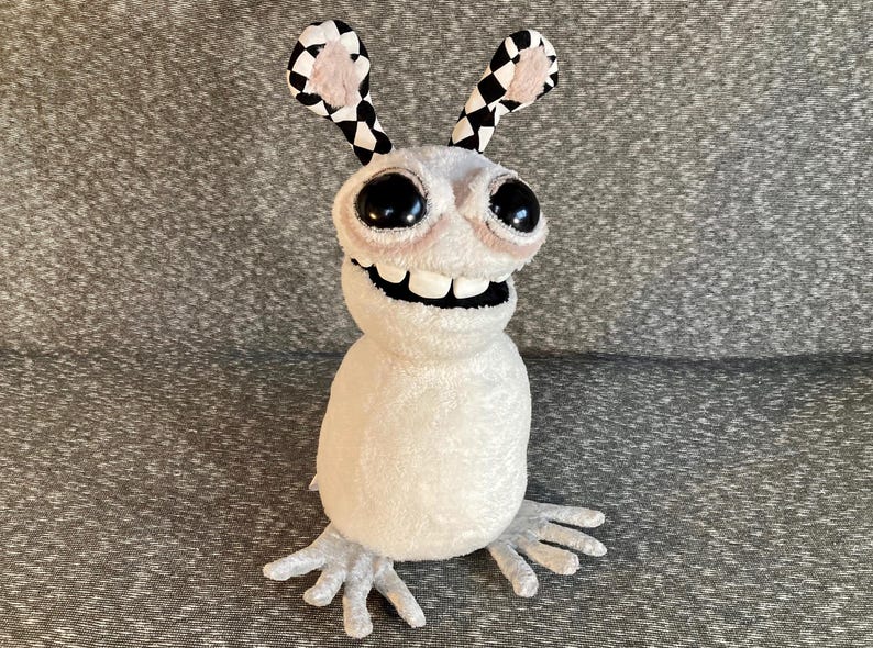 Peut inclure: Un jouet en peluche blanc avec de grands yeux noirs et un large sourire. Le jouet a des oreilles &agrave; carreaux noirs et blancs et de longs bras et jambes blancs &agrave; griffes.