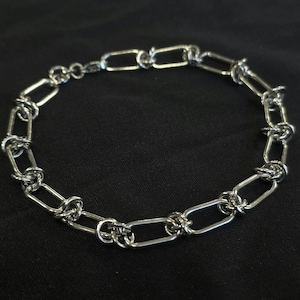 May include: A silver-colored bracelet with a chain link design. The bracelet features a series of interconnected, elongated oval links, with smaller, decorative links between each oval. The bracelet is displayed against a black background.