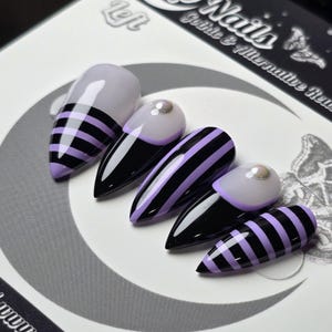 May include: Set of five artificial nails with a black and lavender color scheme. The nails feature a variety of designs, including stripes and a pearl accent. The nails are labeled "Left" and "Gothic & Alternative Nails".