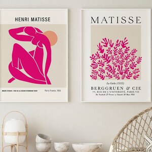 May include: Two framed prints of Matisse artwork. The left print features a pink figure with a peach-colored sun in the background. The right print features a cluster of pink leaves on a beige background. The text on the prints reads "Henri Matisse" and "Matisse".