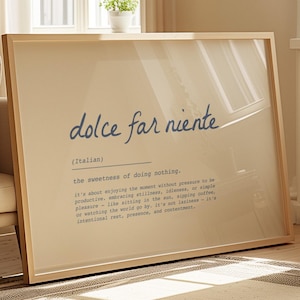 以下が含まれることがあります： 青い筆記体で「dolce far niente」と書かれた額入りのプリント。下のテキストは、何もしないことの甘さを説明しています。フレームは明るい色で、プリントは明るい部屋に表示されています。