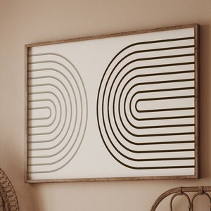 K&ouml;nnte beinhalten: Schlafzimmer-Interieur mit gerahmtem, abstraktem Kunstwerk. Das Kunstwerk hat einen braunen Holzrahmen und zeigt zwei halbkreisf&ouml;rmige Designs in Schwarz und Grau auf cremefarbenem Hintergrund. Ein Pfauenstuhl aus Korbgeflecht und ein Bett mit rostfarbener Decke sind ebenfalls zu sehen.