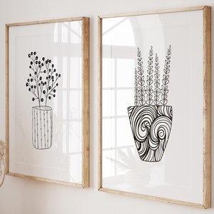 Könnte beinhalten: Zwei gerahmte Schwarz-Weiß-Zeichnungen von Topfpflanzen. Die Zeichnungen befinden sich an einer weißen Wand über einem Holz-Konsolentisch mit Büchern und einem Weidenkorb.