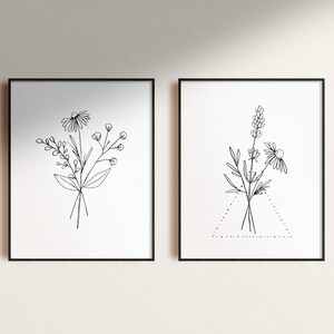 May include: Two black framed prints with white backgrounds featuring line drawings of bouquets of flowers. The print on the left features a bouquet of daisies and other wildflowers. The print on the right features a bouquet of lavender and daisies with a dotted triangle beneath it.