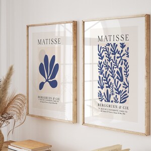 Może przedstawiać: Dwa oprawione wydruki artystyczne z jasnobeżowym tłem i niebieskimi abstrakcyjnymi wzorami kwiatowymi. Wydruki są zatytułowane "Matisse" i zawierają tekst "Berggruen & Cie" z adresem "70 Rue de l'Universit&eacute;, Paris VIIe".