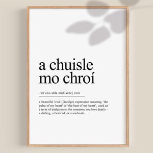 May include: A framed print with the Irish phrase "a chuisle mo chroí" in black text on a white background. The phrase translates to "pulse of my heart" and is a term of endearment. The frame is a light brown color.